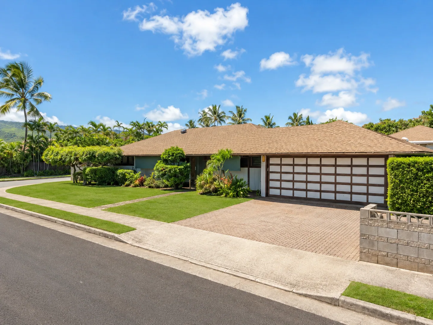 Wide Oahu residential garage door with tropical landscaping.
